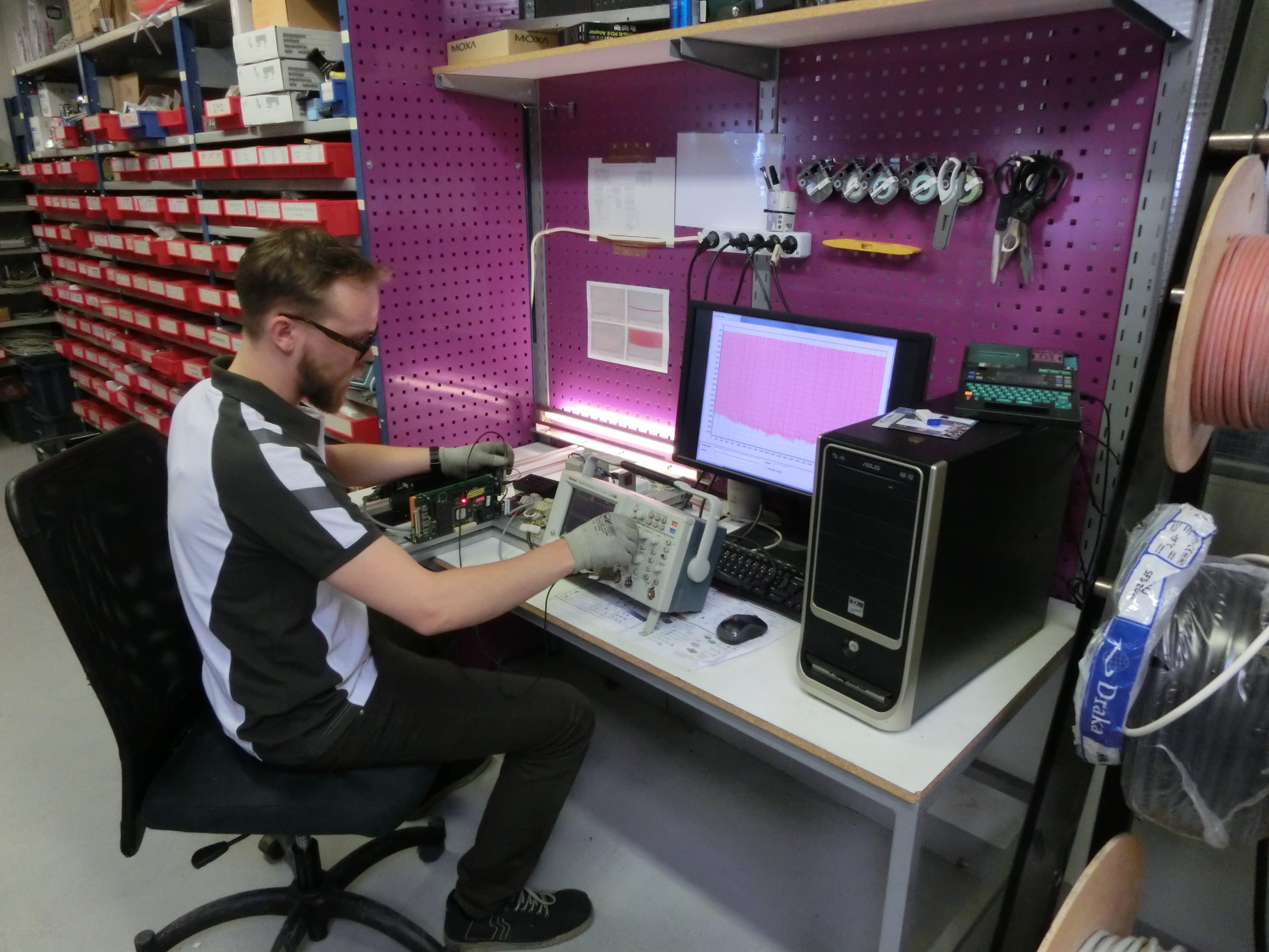Hienomekaniikan kokoonpanoa työpisteellä, taustalla magenta pegboard-seinä